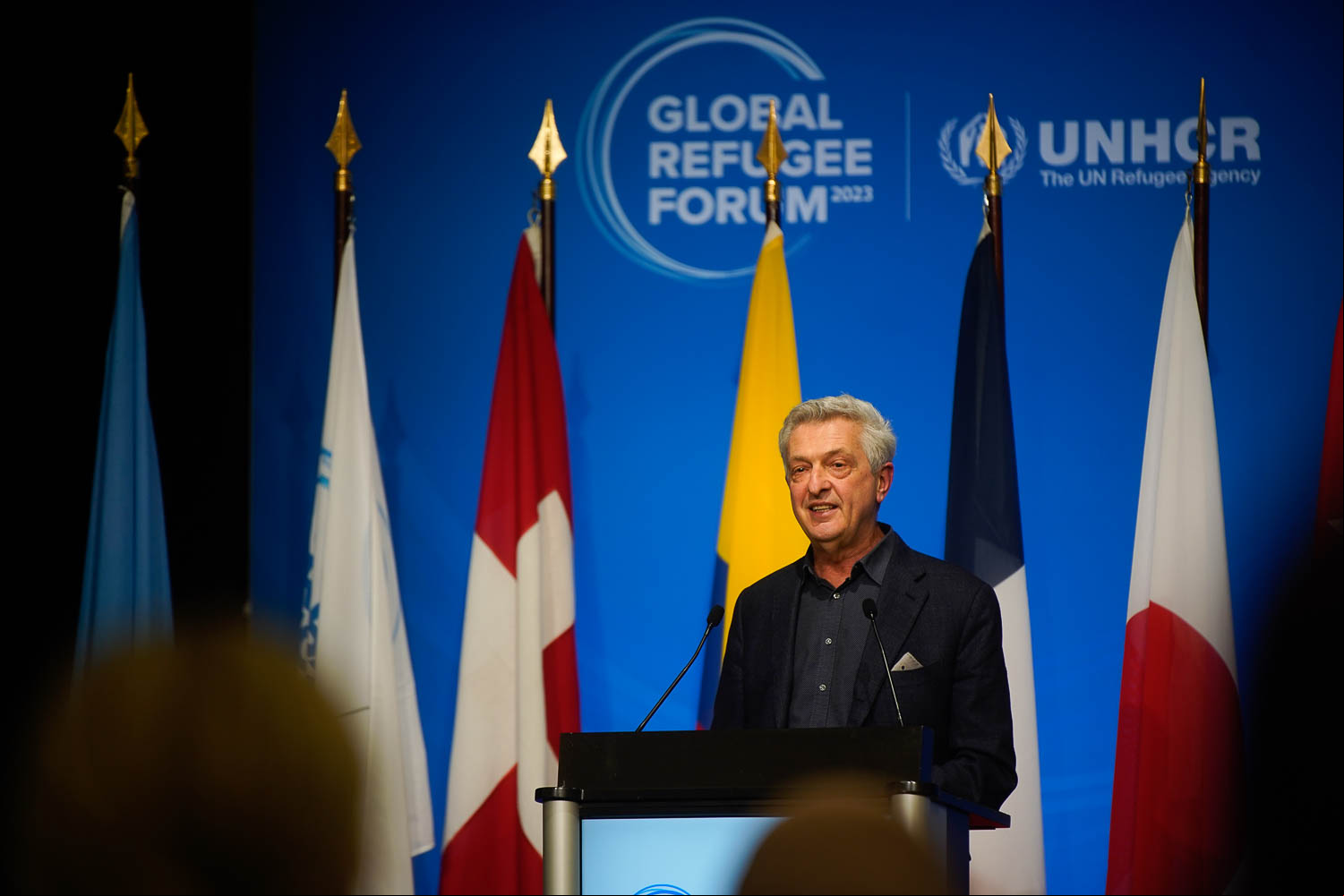 Un hombre cano que lleva puesto un traje emite un discurso desde un podio; detrás suyo, las banderas de diversos países, entre ellos, Canadá.