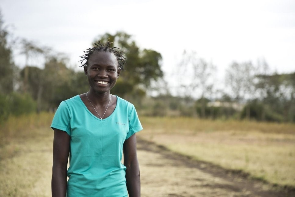 Una mujer sudsudanesa en un terreno con vegetación sonríe a la cámara