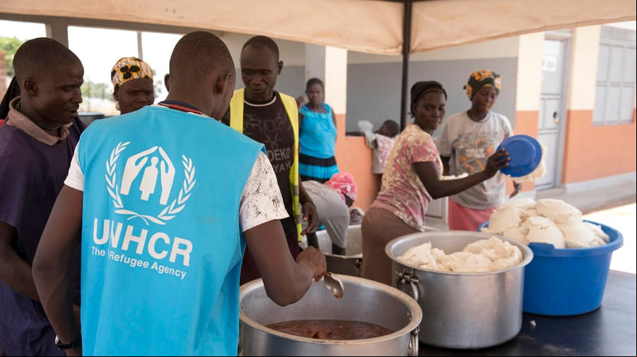 Un grupo de personas se dispone a repartir alimentos. Frente a ellas, un trabajador de ACNUR que lleva puesto un chaleco azul con el logotipo de la organización.