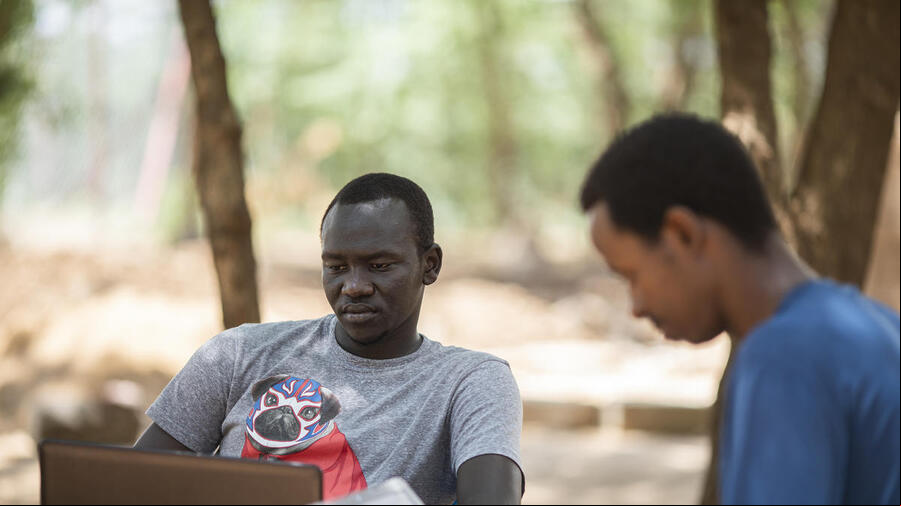 Dos hombres afro estudian en computadores en un parque