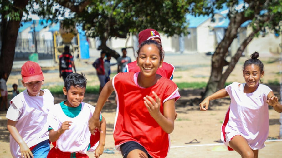 Dos niñas y tres niños corriendo en un parque